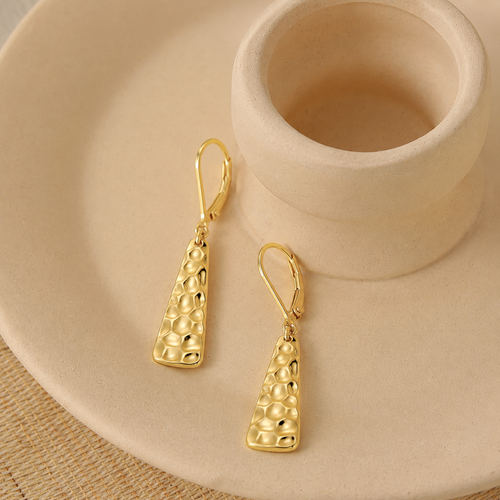 A pair of Elnovaire gold drop earrings with textured triangular pendants, displayed on a beige ceramic dish.