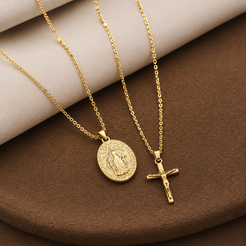 Two Elnovaire gold-tone religious necklaces displayed on a brown and beige fabric surface. One necklace features an oval pendant with a raised figure, and the other features a crucifix pendant.