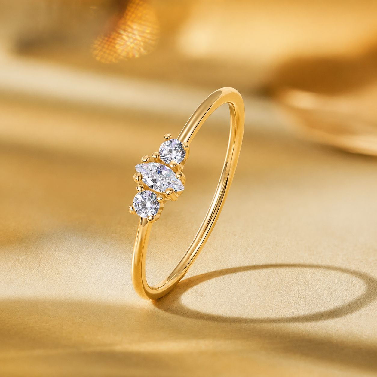 A Elnovaire gold ring with three marquise-cut clear gemstones set in a cluster on a polished gold band, photographed on a warm gold satin surface with a soft blurred background.